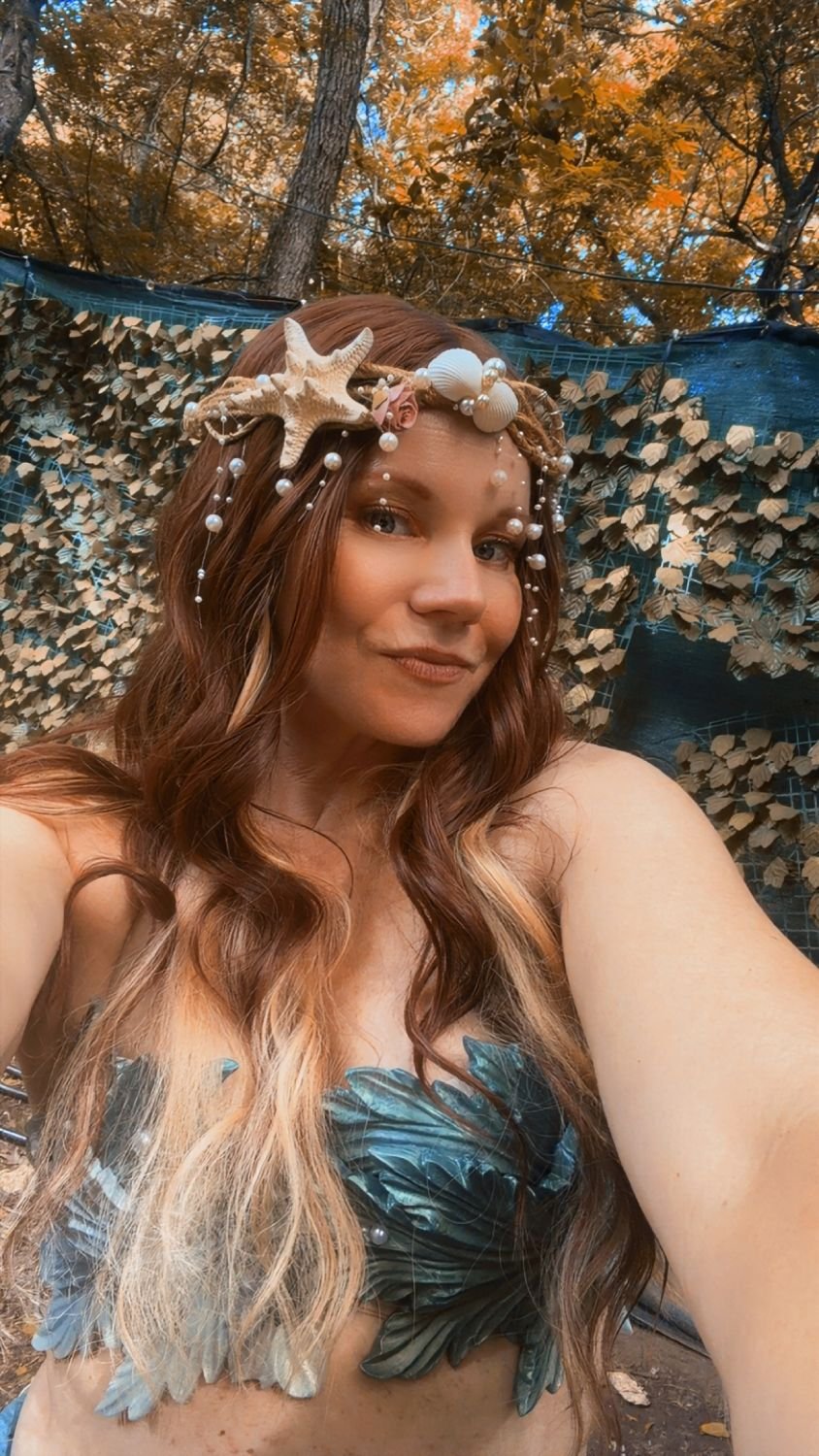 Mermaid performer wearing a seashell and pearl headpiece in an outdoor portrait.