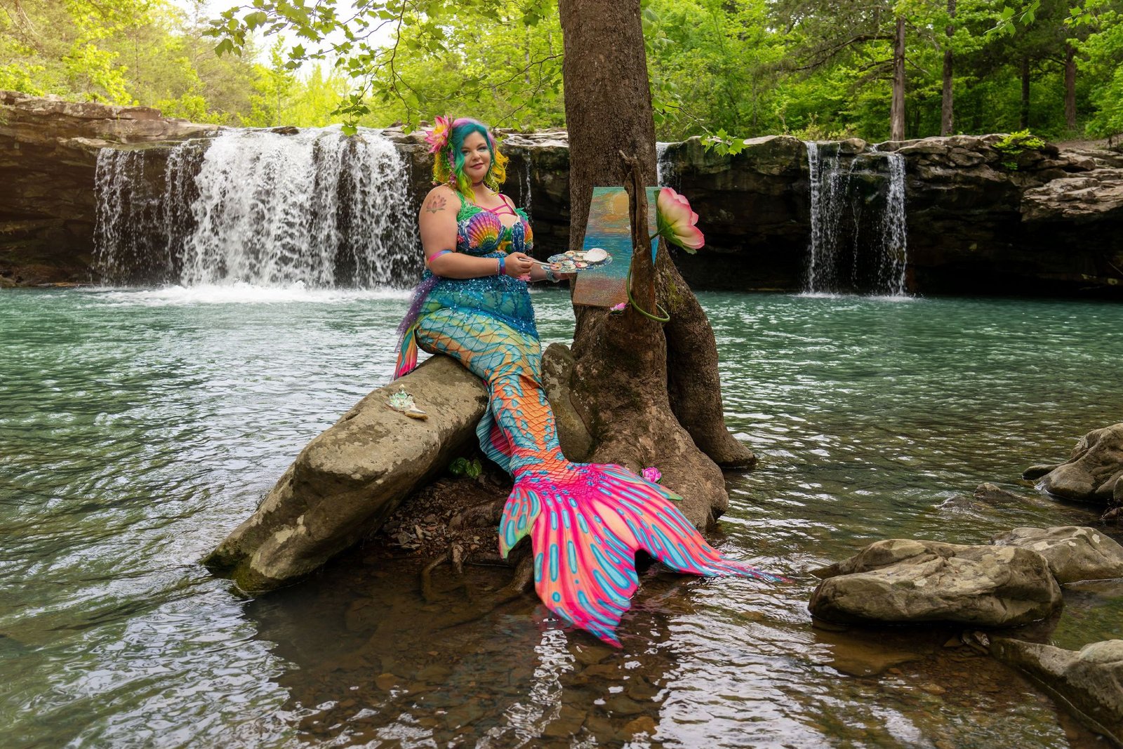 WhimSea Waves posed beside a waterfall in a colorful mermaid tail inspired by her magical paint artistry.